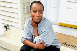 Erica Schwartz sitting on a porch step with a welcoming mat that reads "Home".