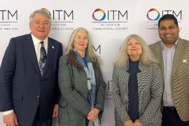 Four people standing in front of a backdrop wth the ITM logo