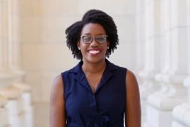 A smiling woman in front of tall architectural columns