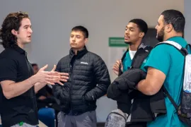 A student gestures with his hands while speaking to three other men wearing scrubs