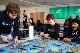 Three people work together making a large blanket