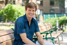 A smiling man seated on an outdoor bench