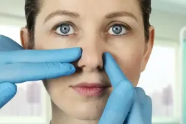 Gloved hands perform an exam on a woman's nose before rhinoplasty, also known as a nose job.
