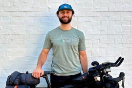 A smiling man wearing a cap and RUSH t-shirt standing beside a bike