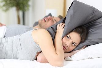 Wman coverin ears with pillow to not hear husband snoring