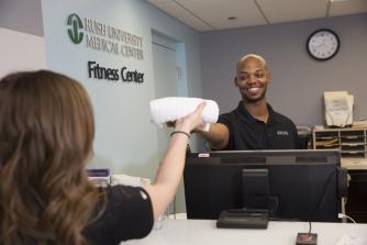 A fitness center employee hands a RUSH employee a towel
