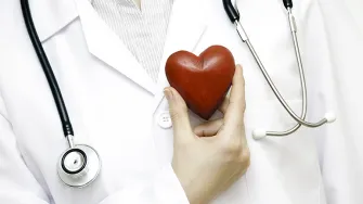 Doctor with stethoscope holding heart near chest