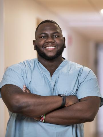 A nurse stands in scrubs with a big smile.