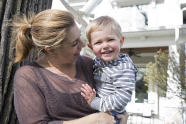 Mother smiles at her smiling toddler son while holding him outside. 