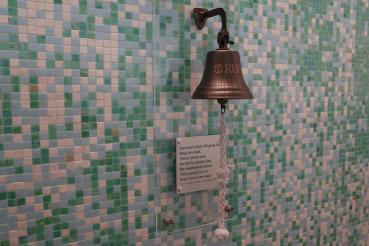 A survivor's bell is pictured on a tiled wall, along with a plaque.