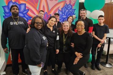 Rush faculty smile in front of a mural in the Cultural Center