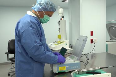 Someone in a gown and mask stands at a machine.