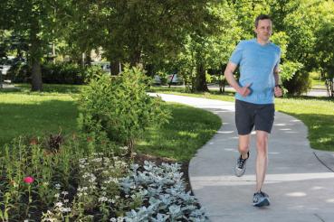 A man runs down a path, with greens and flowers blooming around the path.