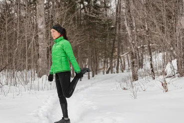 A woman in a green jacket stretching in the snow