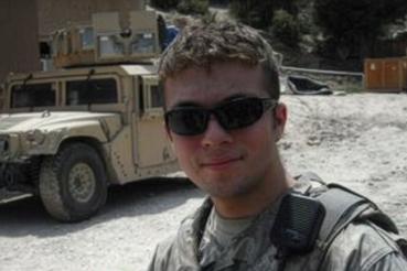 A man wearing mlitary gear and wearing sunglasses stands near a a military vehicle.