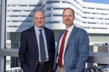 George Fitchett, co-founder and senior advisor for Transforming Chaplaincy, stands at the left, while Csaba Szilagyi, director of Transforming Chaplaincy, stands to the right, with Rush University Medical Center's hospital tower in the background.