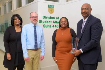 Four people standing in front of a wall sign that reads Division of Student Affairs