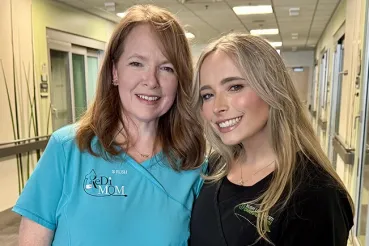 An older woman and a younger woman smile at the camera inside the NICU
