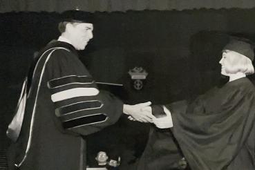 Black and white photo of a graduate receiving a diploma