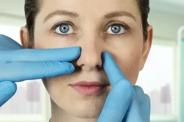 Gloved hands perform an exam on a woman's nose before rhinoplasty, also known as a nose job.