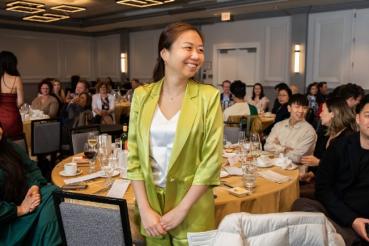A smiling woman stands in the middle of a crowded banquet room