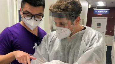 Two medical professionals wearing masks consult paperwork
