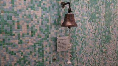 A survivor's bell is pictured on a tiled wall, along with a plaque.