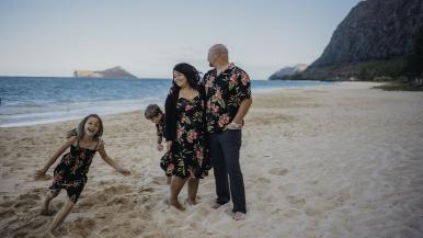 Fitha Dahana-Ellis stands on the beach with her husband and two children, who are running in the sand.