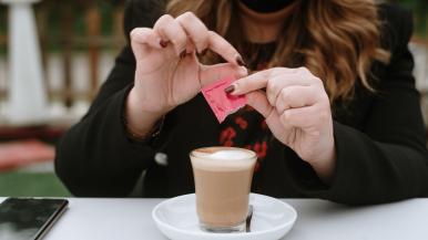 Young woman opening artificial sweetener packet to add to coffee