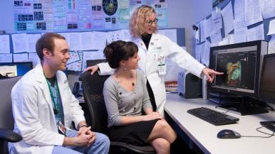 Three medical professionals examine a diagnostic image on screen