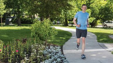 A man runs down a path, with greens and flowers blooming around the path.