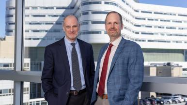 George Fitchett, co-founder and senior advisor for Transforming Chaplaincy, stands at the left, while Csaba Szilagyi, director of Transforming Chaplaincy, stands to the right, with Rush University Medical Center's hospital tower in the background.
