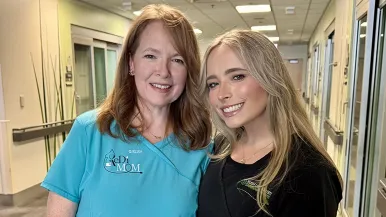 An older woman and a younger woman smile at the camera inside the NICU