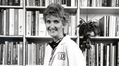 Kay Andreoli wearing a white coat and standing in front of a wall of bookshelves