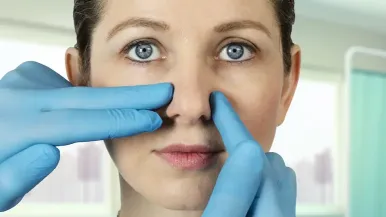 Gloved hands perform an exam on a woman's nose before rhinoplasty, also known as a nose job.