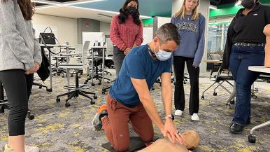 man giving CPR to test dummy on the floor as people observe