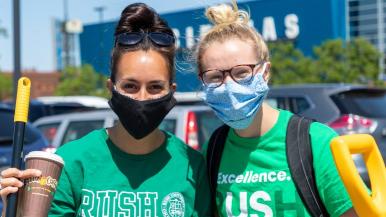 Two students wearing Rush University T-shirts and holding cleaning supplies