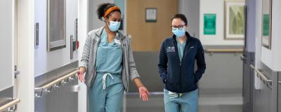 Two labor and delivery residents walk down a hallway talking with each other.
