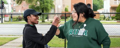 Two people standing outside, smiling and high-fiving
