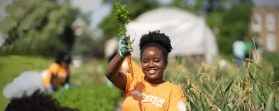 A woman harvesting produce in a field holds up a carrot