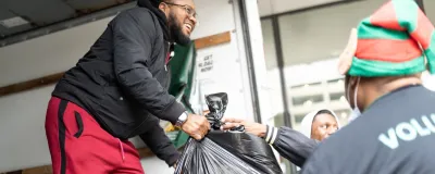 A smiling man in the back of a truck hands a full bag of gifts to waiting volunteers