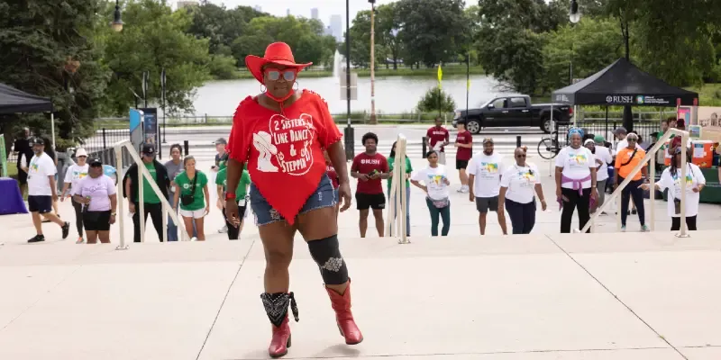A woman wearing matching red t-shirt, cowboy hat and boots stands in front of a group of people